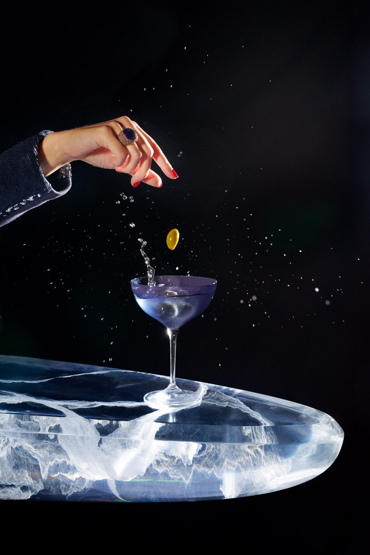 cocktail dry martini sobre fundo preto com uma mão fazendo cair azeitonas