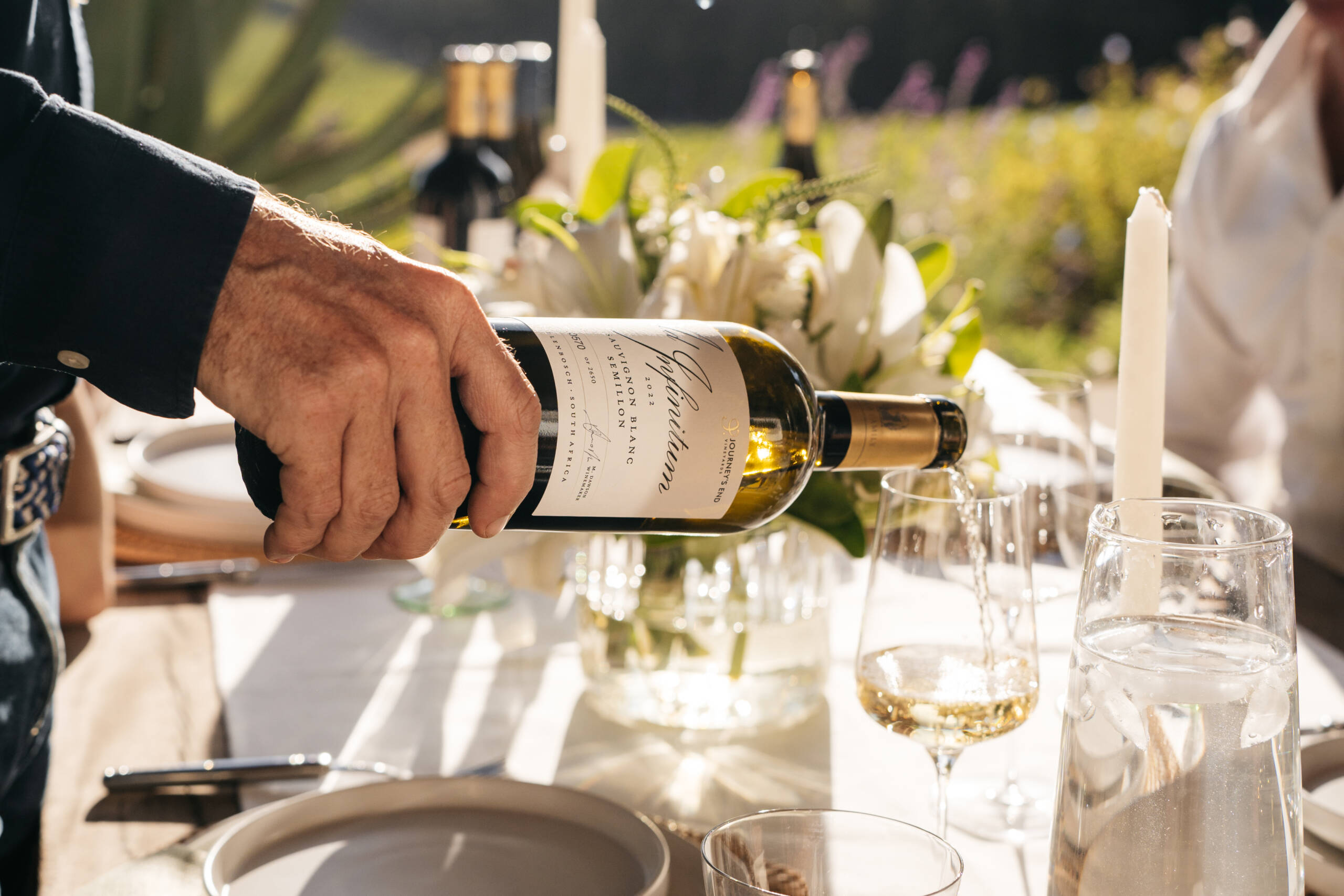 The host pouring a glass of white in a wine dinner outdoor set up.