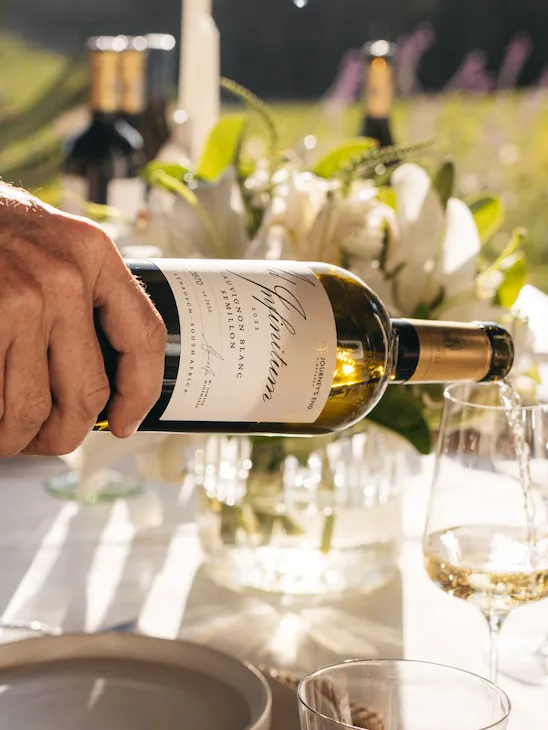 The host pouring a glass of white in a wine dinner outdoor set up.