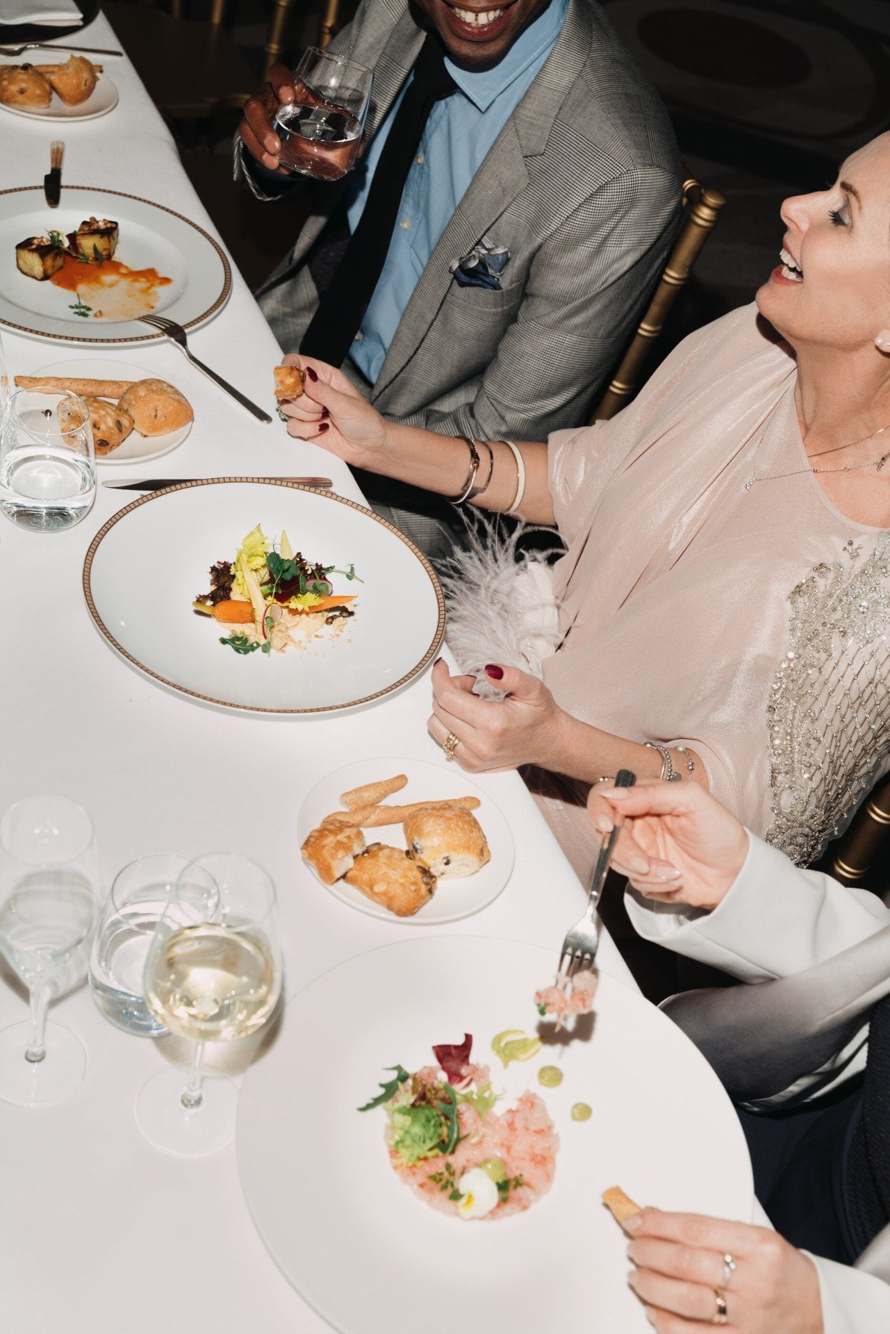 Dettaglio di un tavolo durante una cena di gala con persone che mangiano e bevono vino, con dettaglio di fiori in primo piano