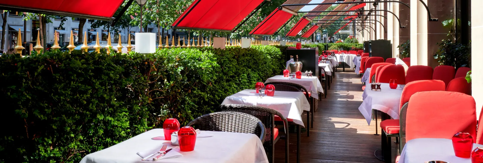 Terrasse Montaigne avec tables dressées, sièges rouges iconiques et auvents à l'hôtel Plaza Athénée, Paris