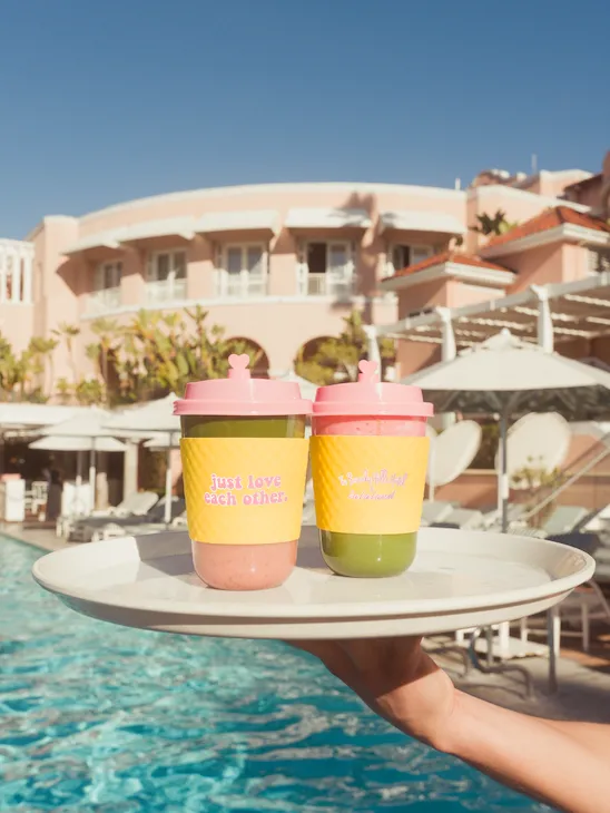Two matcha lattes on a tray in front of the Beverly Hills Hotel pool with hotel in background and blue skies