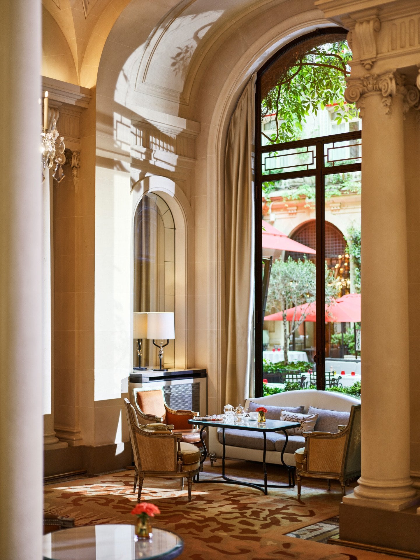 Table à manger à la galerie, table avec tasses de thé, deux fauteuils et un canapé à côté d’une fenêtre ensoleillée donnant sur la cour Jardin, à l’Hôtel Plaza Athénée, Paris
