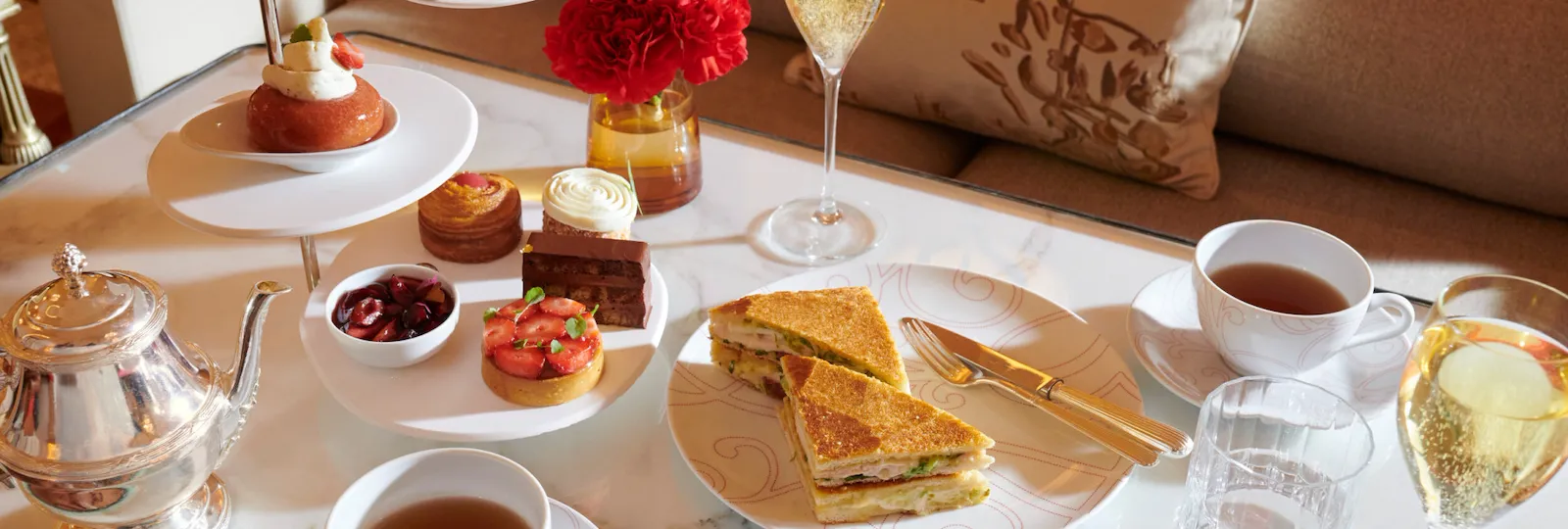 La Galerie Tea Time avec une sélection de pâtisseries signature d’Angelo Musa, un club sandwich traditionnel, du thé et du champagne, sur une table en marbre, à l’Hôtel Plaza Athénée, Paris