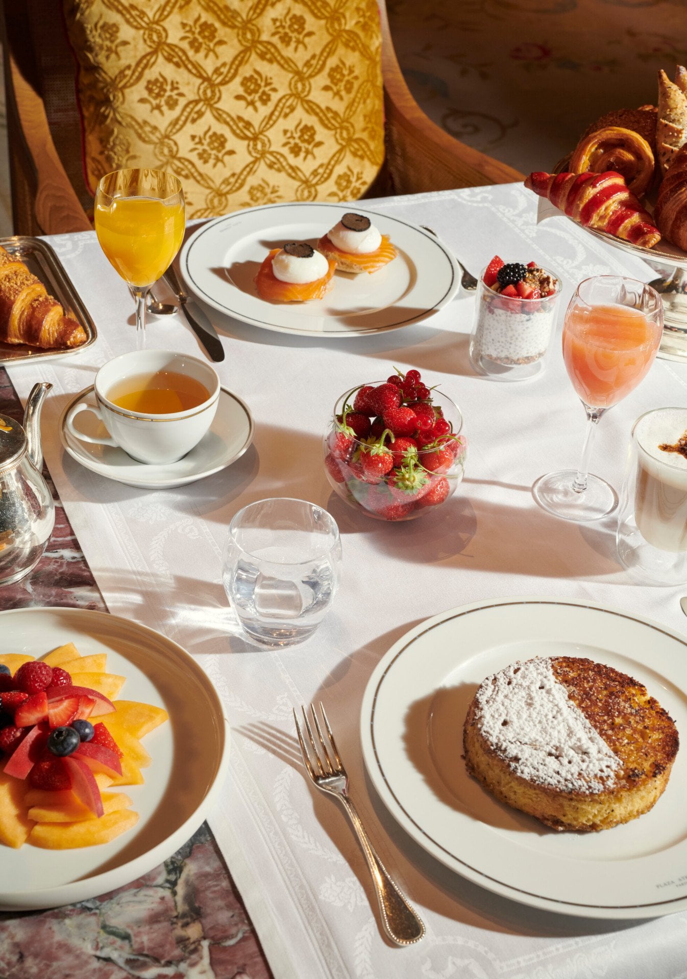 Imagens do brunch no quarto Imagens do brunch no Jean Imbert au Plaza Athénée. Podemos ver uma salada de frutas, bolos, café, ovos e sucos

