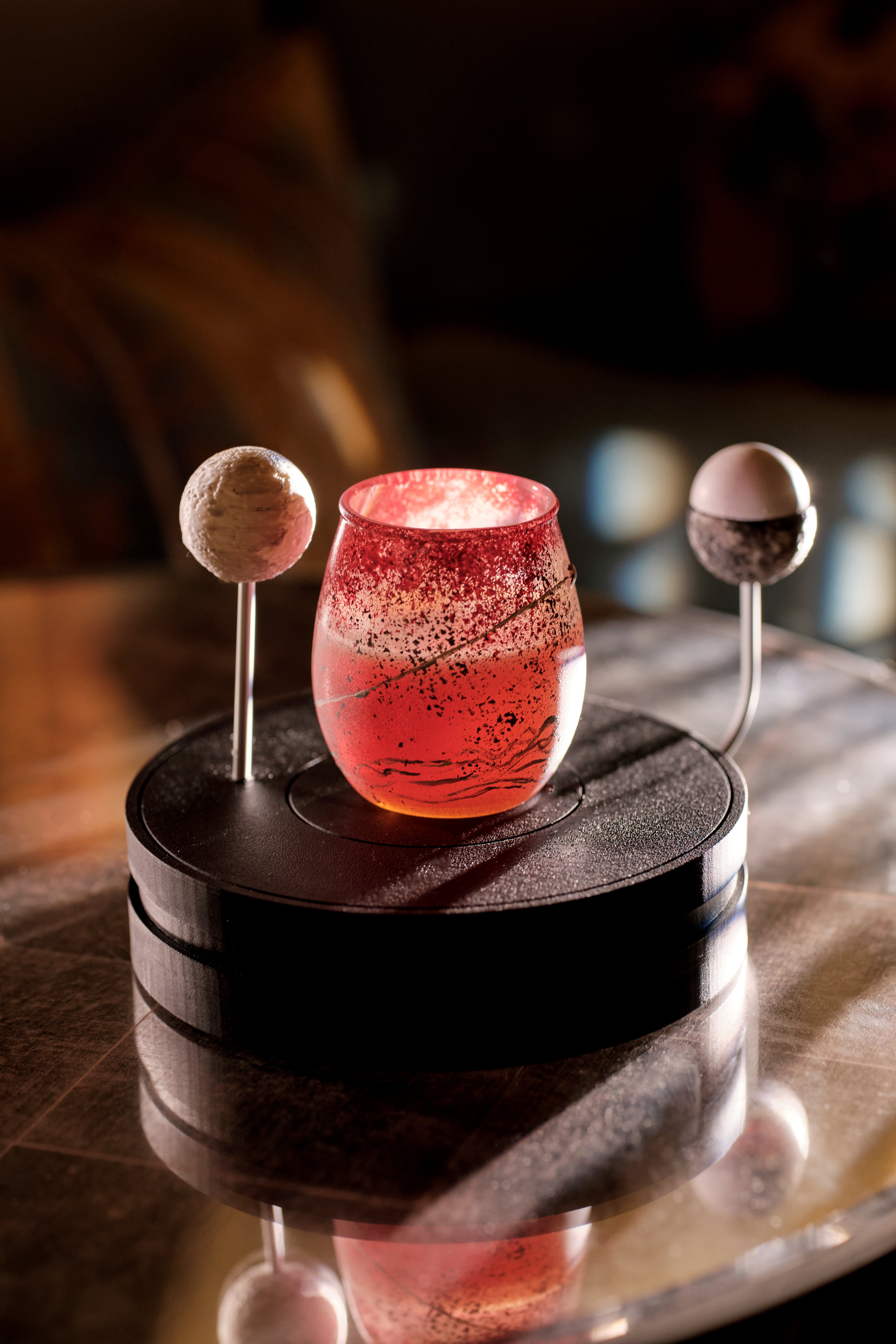 A pink cocktail from The Vesper Bar’s Planetarium menu, presented with celestial-inspired garnishes on a sculptural display stand.