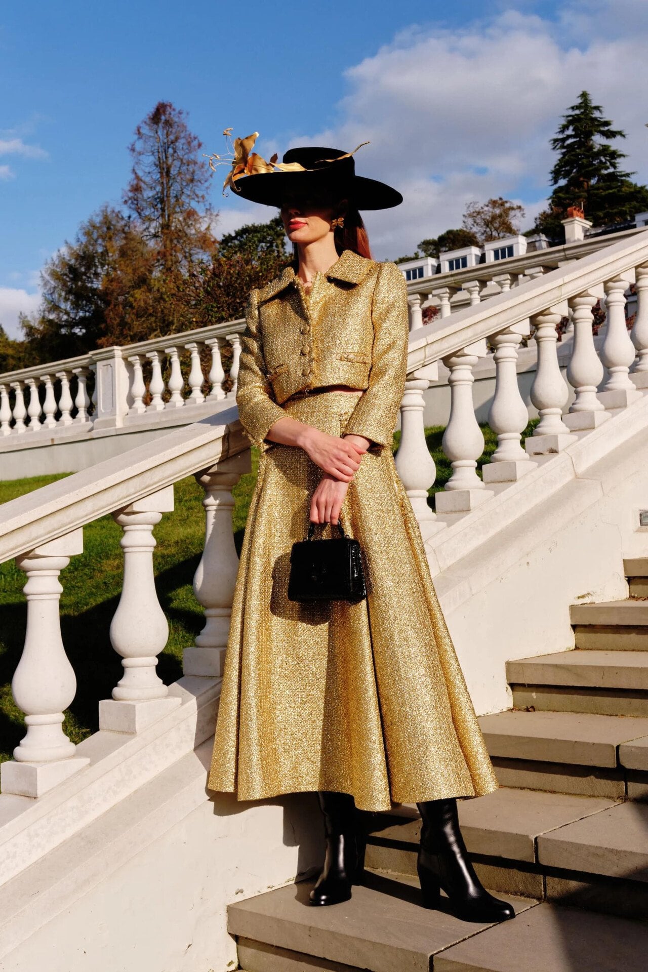 A person in a hat and gold skit standing on the stairs that lead from the croquet lawn to the rose garden in the Grounds of Coworth Park