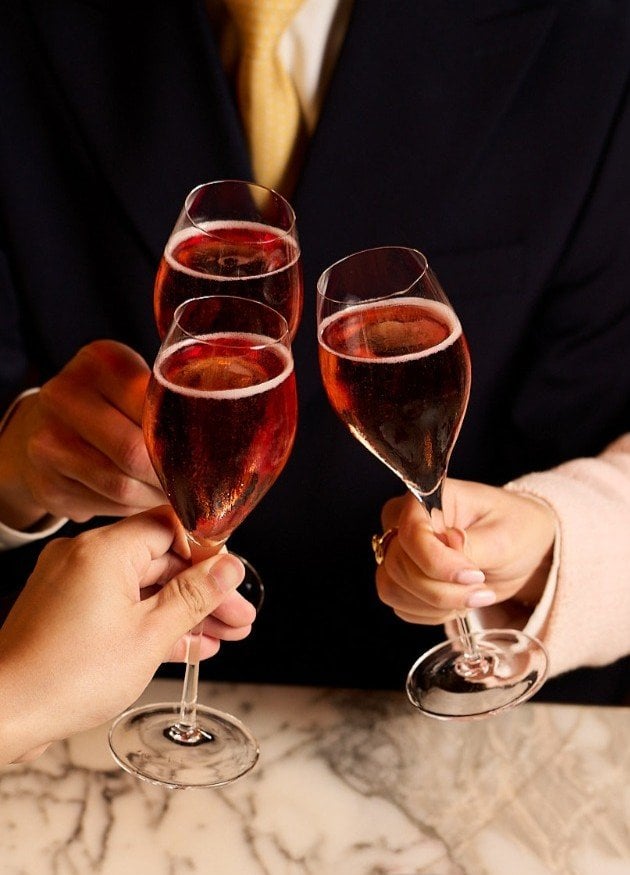 People clinking glasses of sparkling wine in a celebration setting with a marble surface.