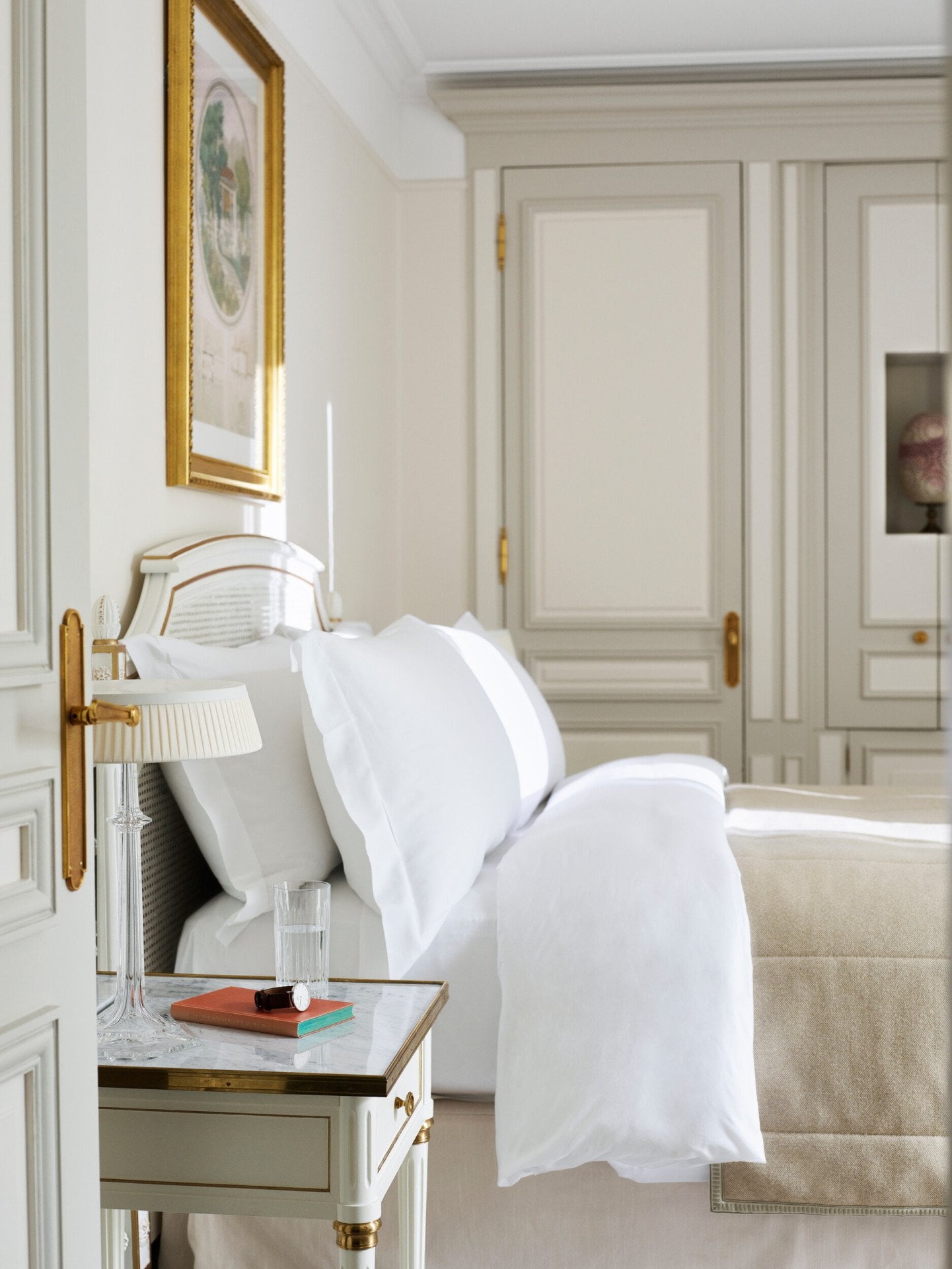 Quarto em tons de bege e branco com armário de madeira ao fundo e cama queen. No Le Meurice, Paris.