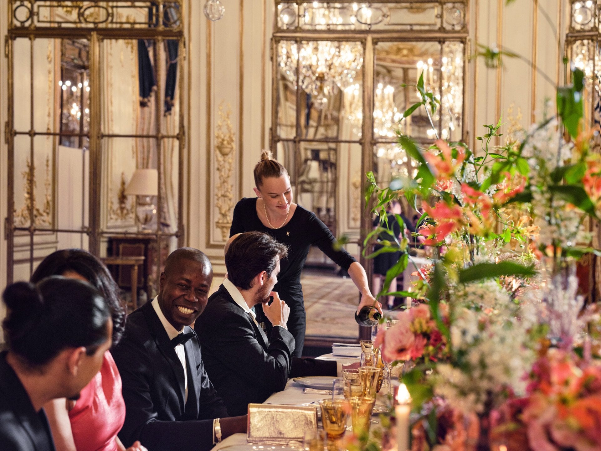Women serving champagne to guests, sitting at the table, during a dinner in Le Salon Pompadour at Le Meurice, Paris - Dorchester Collection