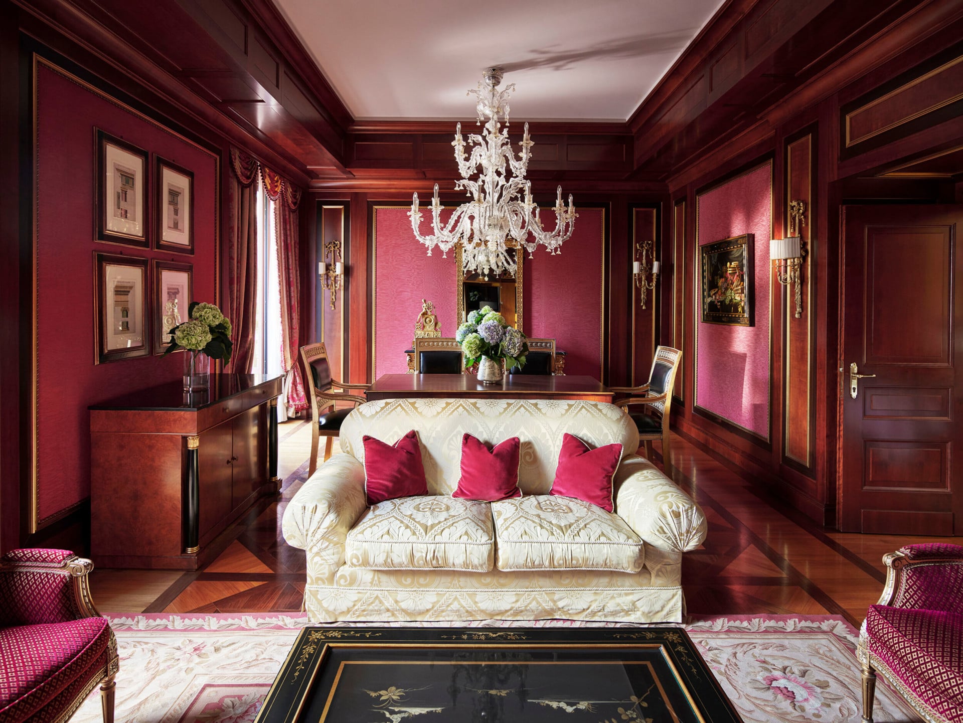 Panoramica del soggiorno della Royal Suite con un arredamento prevalentemente rosso e un divano bianco in primo piano.