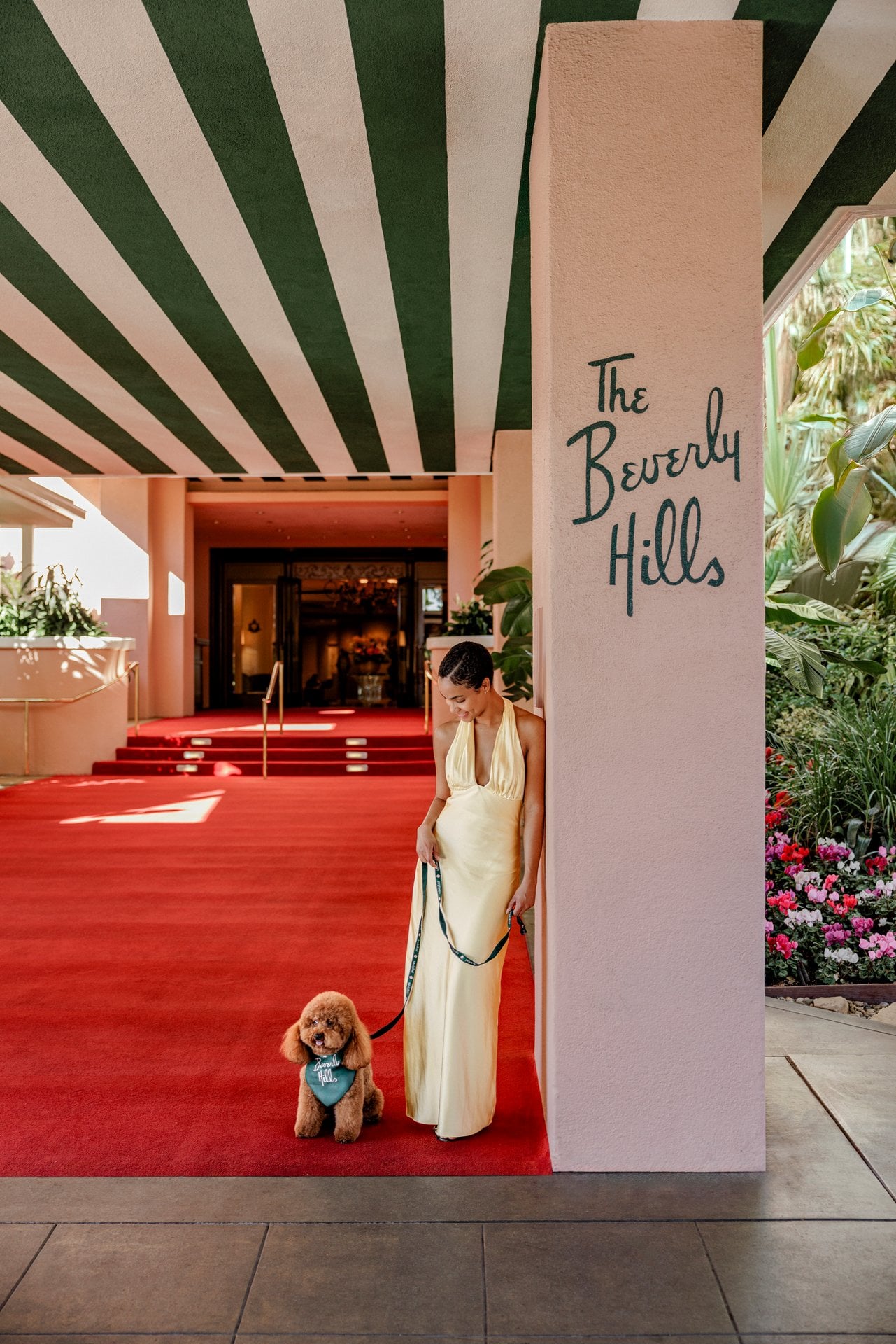 A person with a service dog by a building entrance, sunny day, relaxed mood, lush greenery around