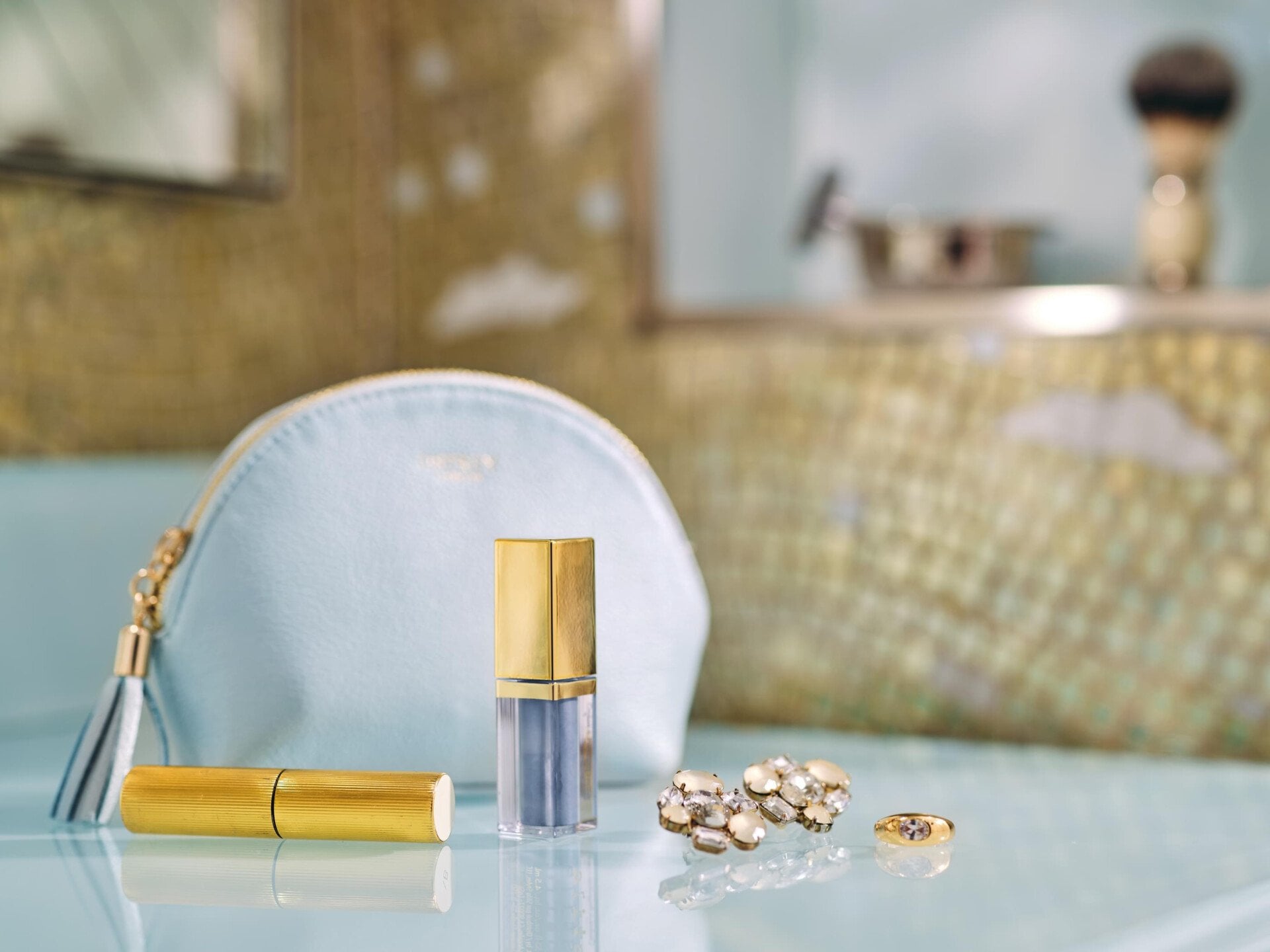 pochette azzurra con rossetto e orecchini oro appoggiati in bagno 