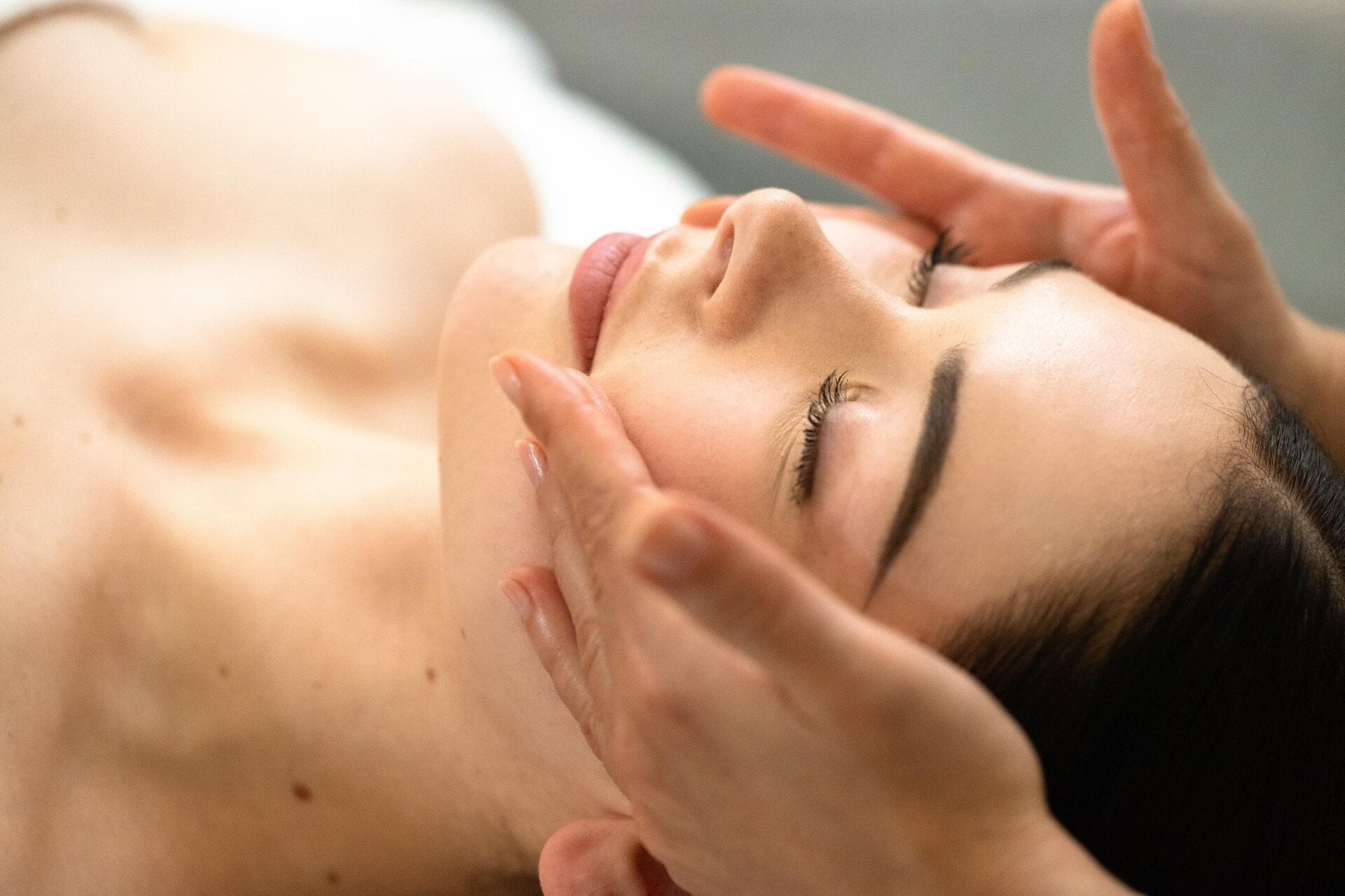We can see the masseuse's two hands on the client’s cheeks. Her eyes are closed. We can see a focus on the client’s face at Le Meurice, Paris.
