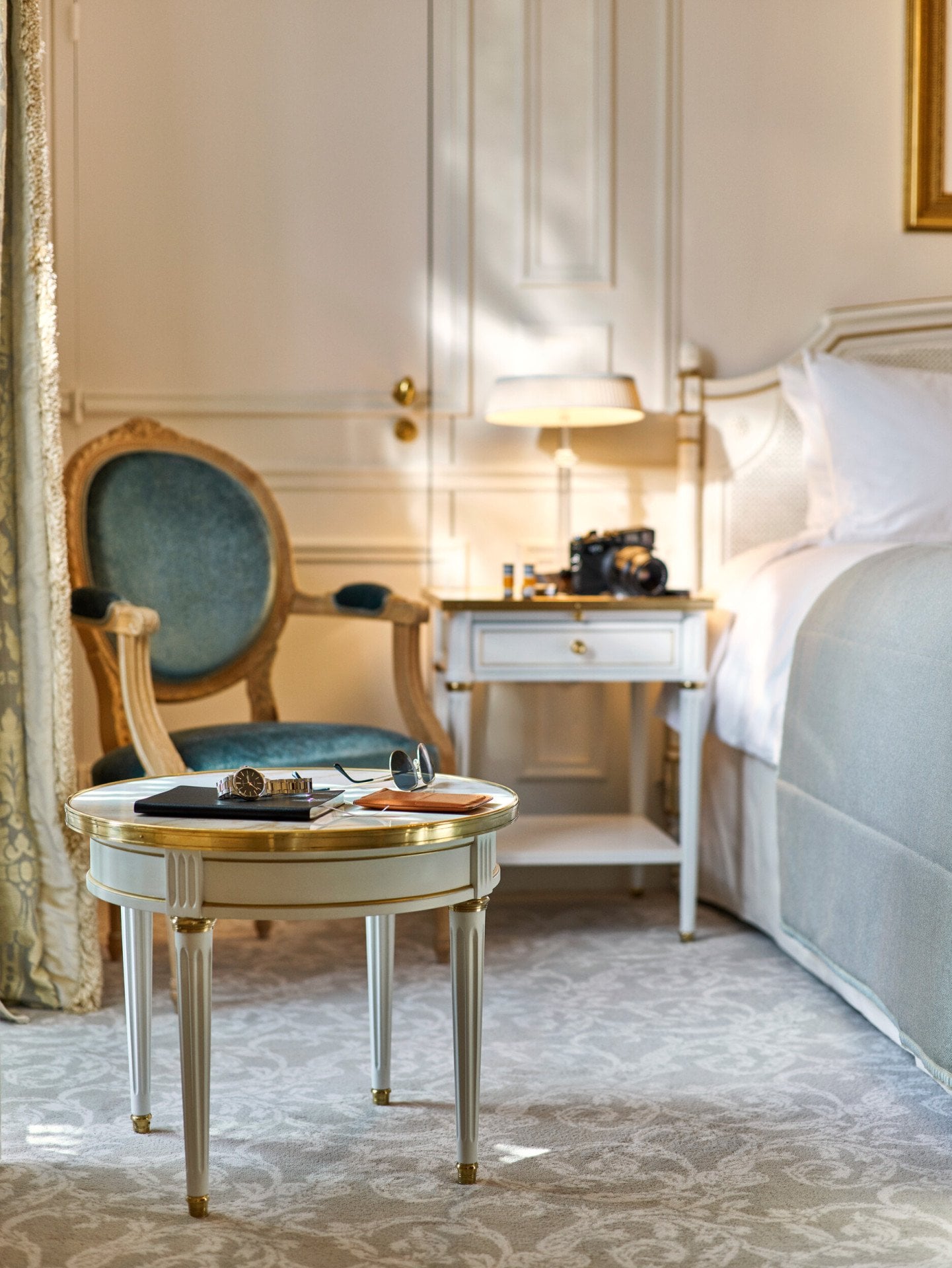 Óculos de sol, um relógio e um bloco de notas colocados numa mesa junto à cama num quarto executivo. No Le Meurice, Paris.