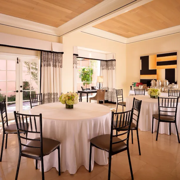 Three round tables and chairs with floral centerpieces set up inside a bright, spacious Hospitality Suite