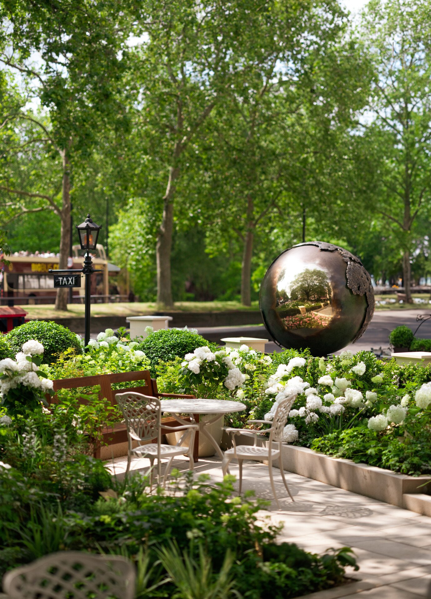 The Dorchester Garden, featuring the hotel's iconic reflective globe sculpture surrounded by white flowers, manicured planting and elegant outdoor seating overlooking Hyde Park.