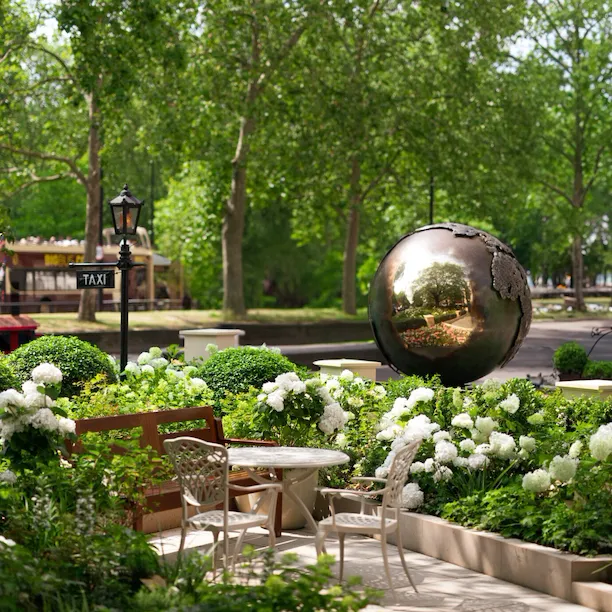 The Dorchester Garden, featuring the hotel's iconic reflective globe sculpture surrounded by white flowers, manicured planting and elegant outdoor seating overlooking Hyde Park.