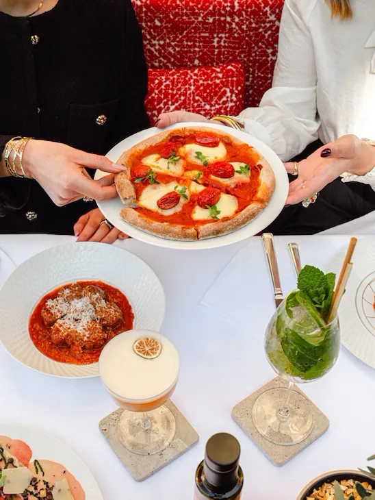 two aldies sidding at a table sharing a pizza with tomato and mozzarella