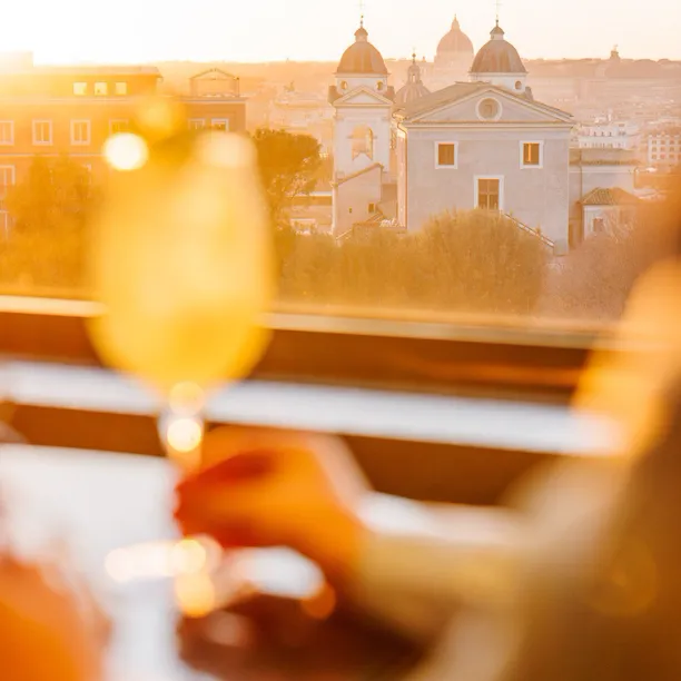 Figura di donna che tocca un calice con un cocktail e sullo sfondo la vista sulla cupola di San Pietro da Il Giardino bar