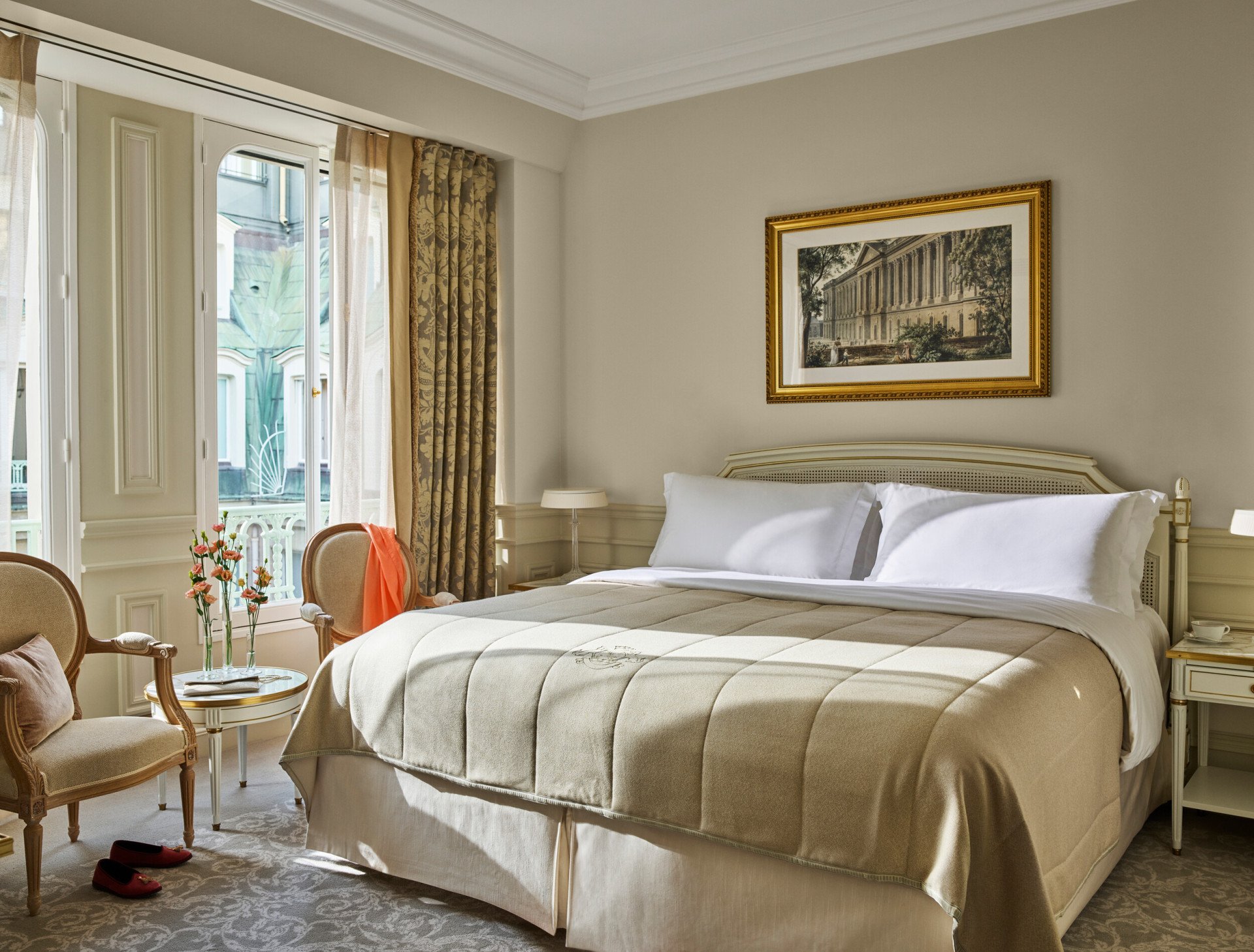 Quarto superior em tons de bege e branco com cama queen e flores sobre mesa baixa, no Le Meurice, Paris.