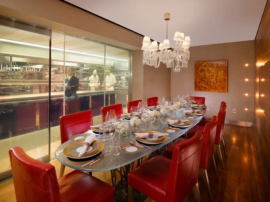 Chef's Table private dining area with view into the kitchen. Table set for 10 peope with gold and white table settings and floral arrangements.