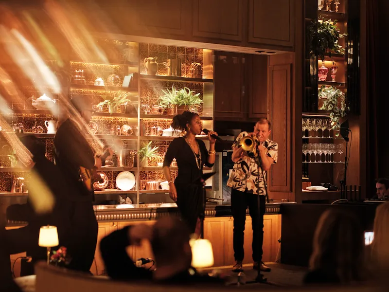 Live music at Ronnie Scott’s at The Dorchester, showcasing musicians performing on stage in front of a mirrored back bar, with warm lighting and guests seated throughout the intimate venue.