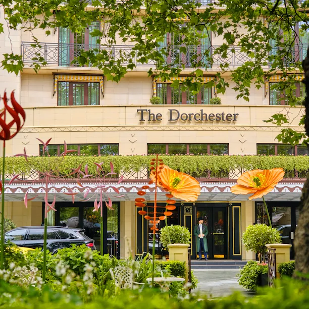 The La DoubleJ summer garden at The Dorchester with external view of the hotel. Large orange flowers and sculptures full the green and leafy alfresco dining area in Mayfair.