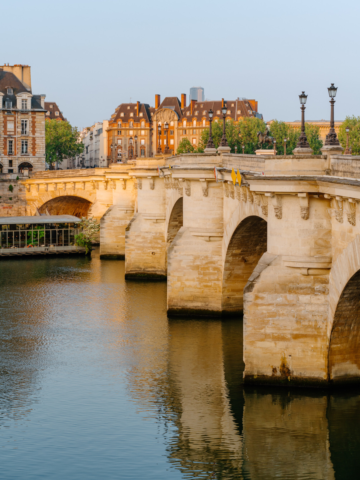 Global view of le Pont Neuf at sunrise with the reflection of the bridge in the water. Orangey buildings in the back of the picture, at Pont Neuf, Paris.