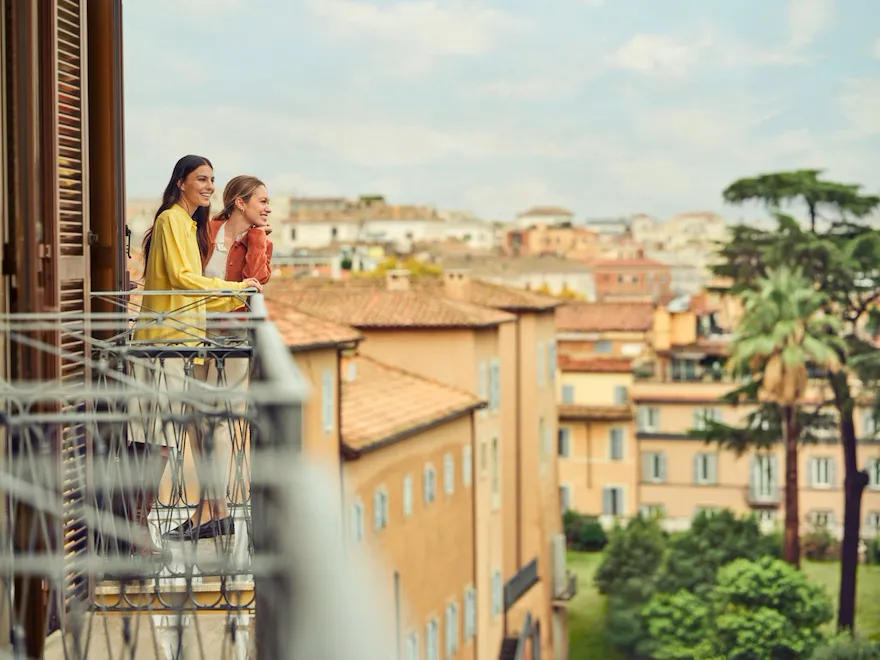 Due giovani donne sorridenti che ammirano la vista su Roma da un balcone di Hotel Eden