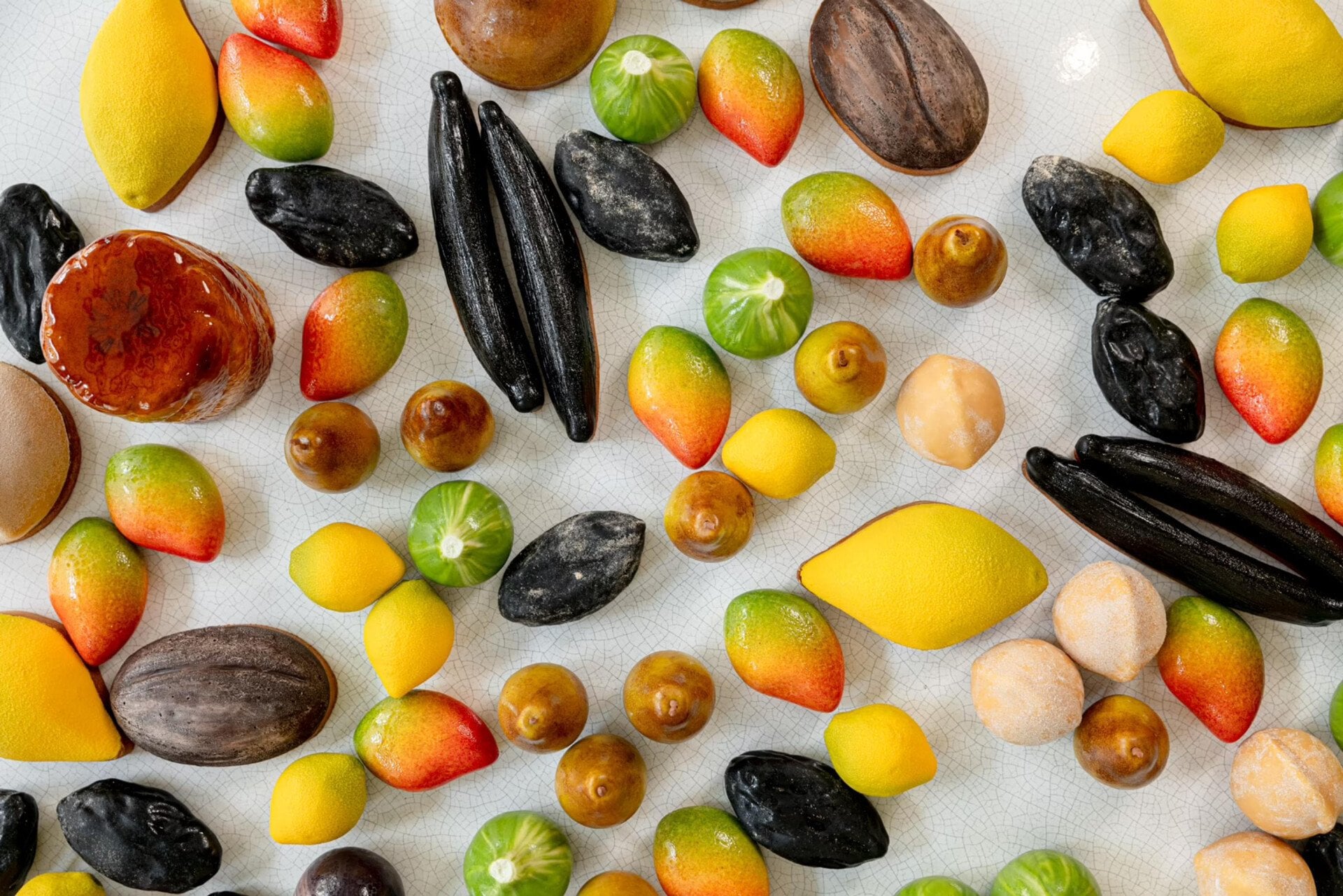 Des fruits colorés assortis, notamment des citrons, des oranges et des citrons verts, mélangés à des gousses de vanille noire, sont dispersés sur une surface claire, créant un arrangement frais et éclatant.