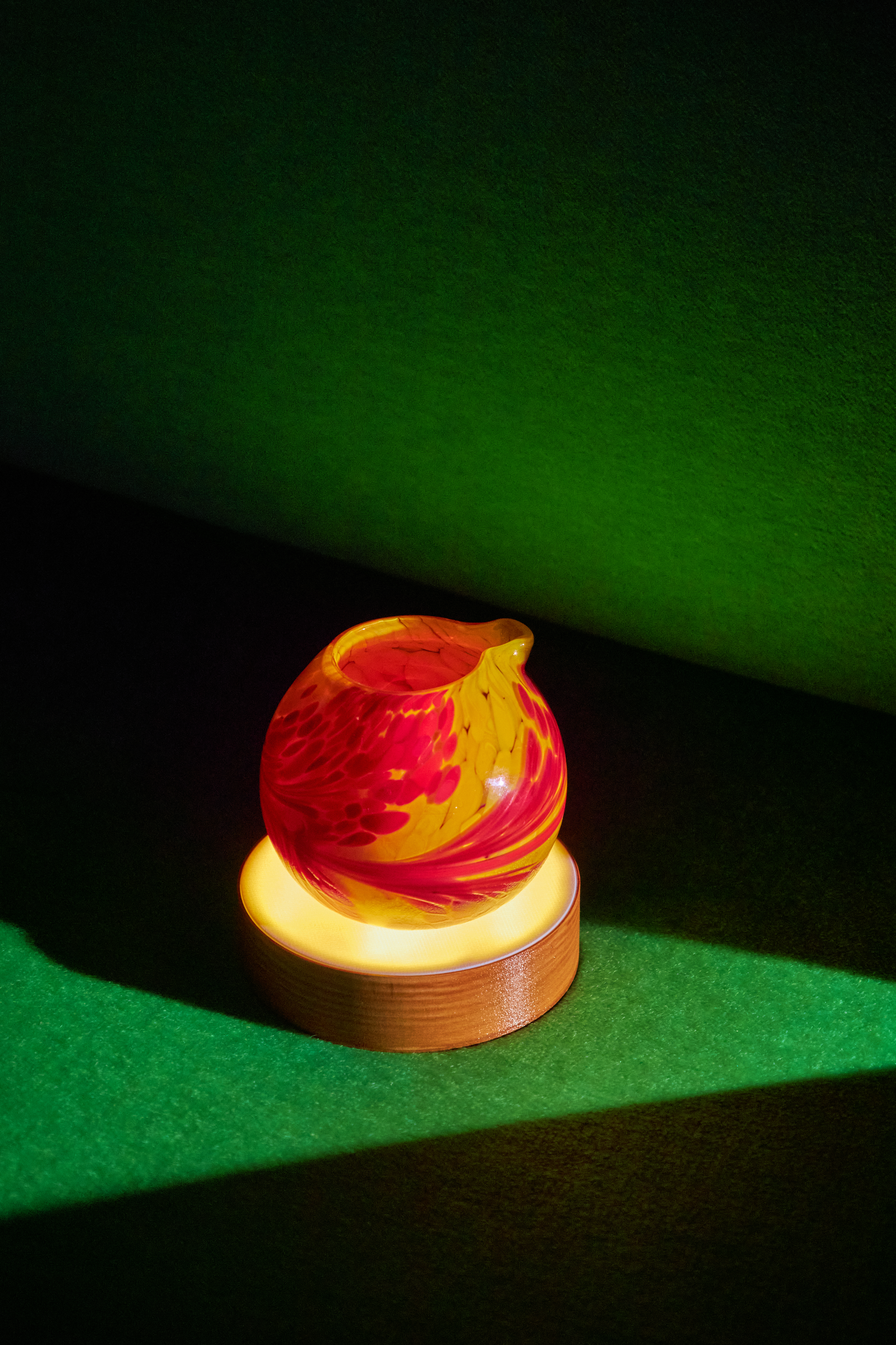 A glowing red and amber glass vessel presented as part of the Planetarium menu experience at The Vesper Bar, illuminated against a deep green backdrop.