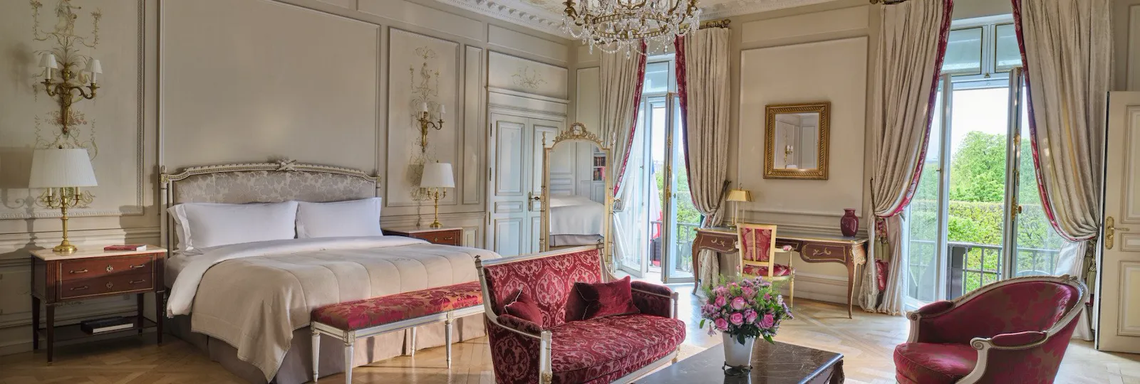 Vista ampla da Suíte Presidencial Dali com em primeiro plano os móveis de uma sala de estar, como sofá, carpete e cadeiras, e ao fundo a cama e o espelho, no Meurice, Paris
