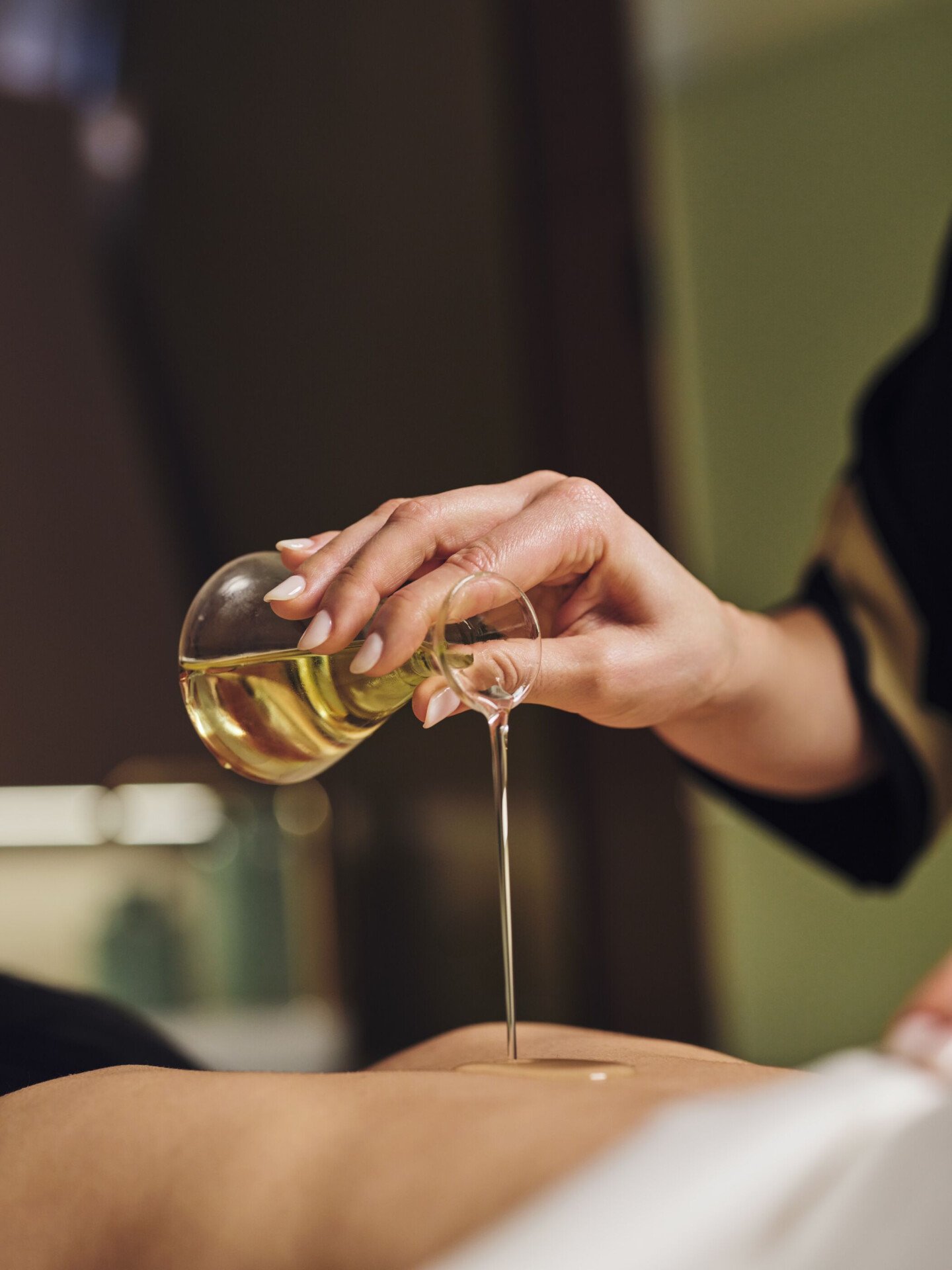 Mano che versa da una bottiglietta di vetro olio sulla schiena nuda di una donna sdraiata su un lettino