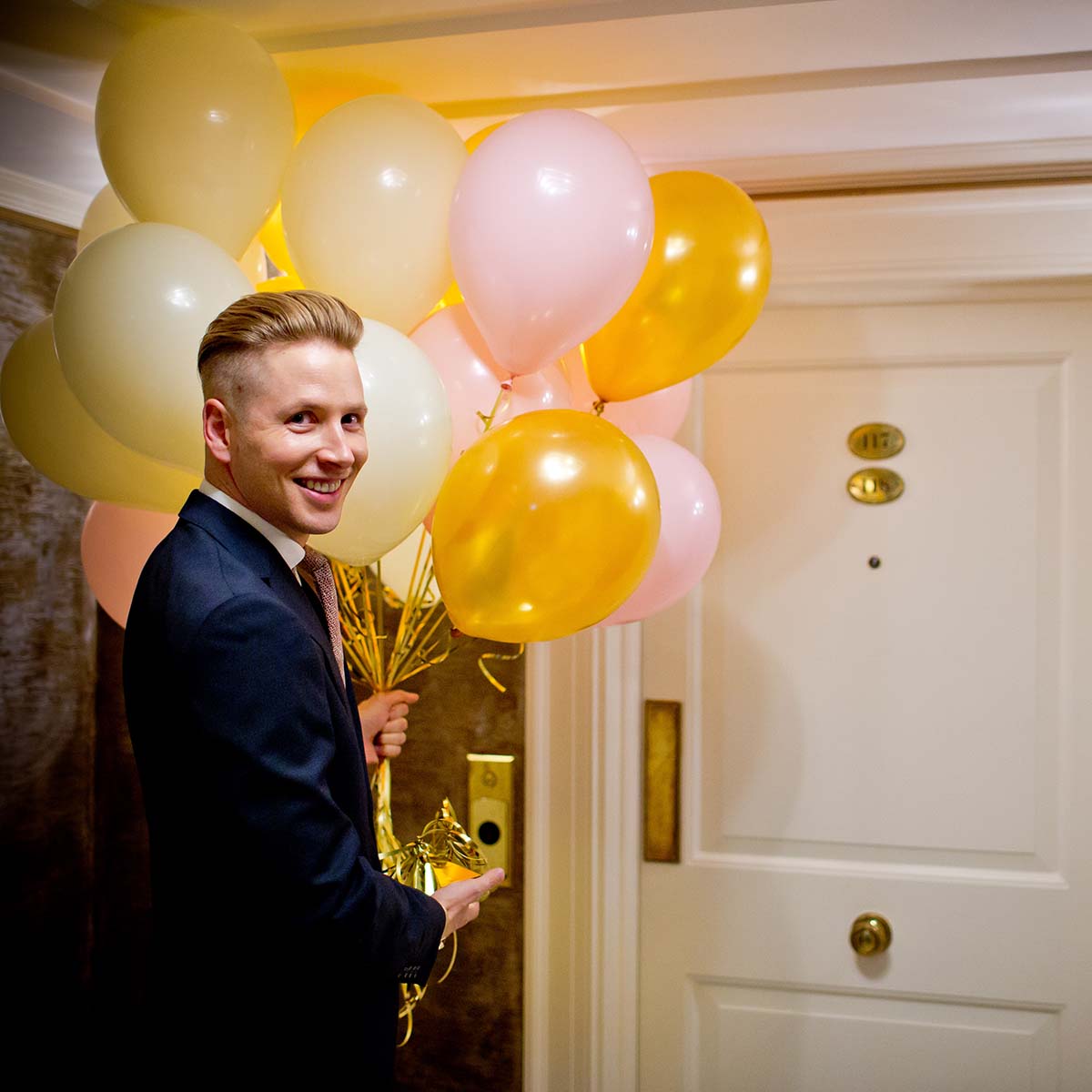 A guy holding balloons in front of the hotel room