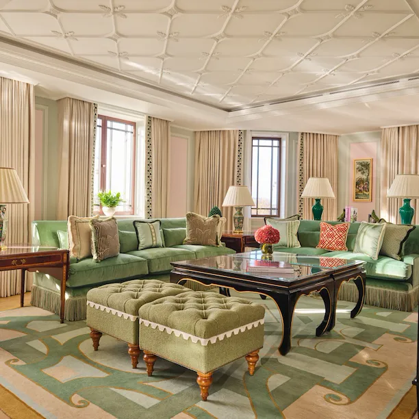 Elegant living room with green sofas, lamps, windows, and decorative rugs creating a cozy atmosphere