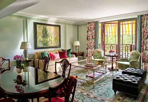 The Belgravia Suite with elegant green and red tones, a comfortable lounge seating area, dining space and a Juliet balcony offering views across Hyde Park and Park Lane.