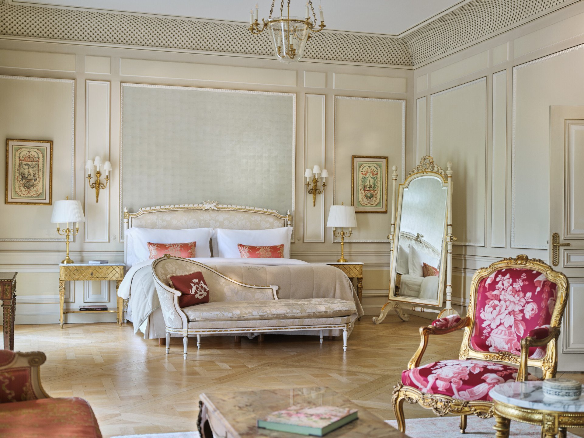 Quarto elegante com decoração vintage. Possui uma cama luxuosa, espelho ornamentado com moldura dourada, cadeiras florais e iluminação suave, evocando uma sensação clássica e opulenta.