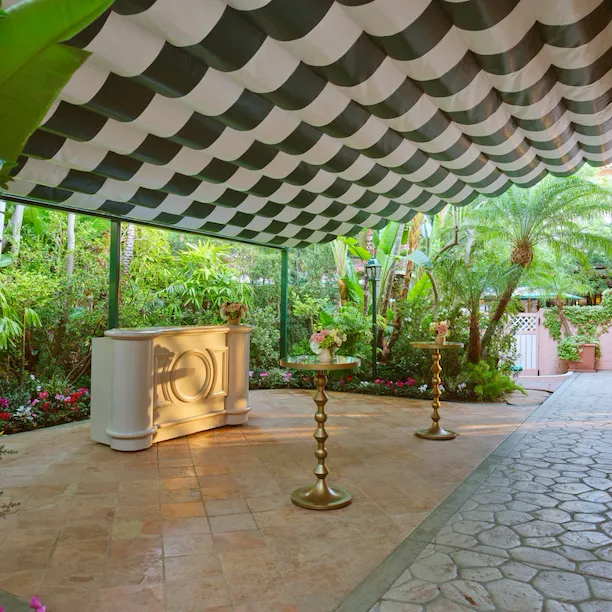 Outdoor garden with columns, plants, and a shaded seating area under a striped awning