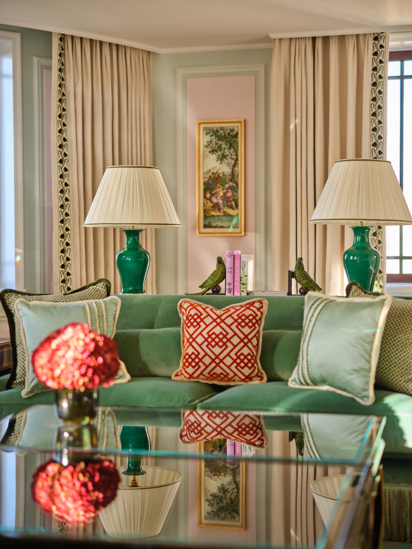 Elegant living room with green sofa, lamps, decorative cushions, and a glass table.