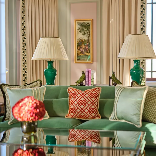 Elegant living room with green sofa, lamps, decorative cushions, and a glass table.