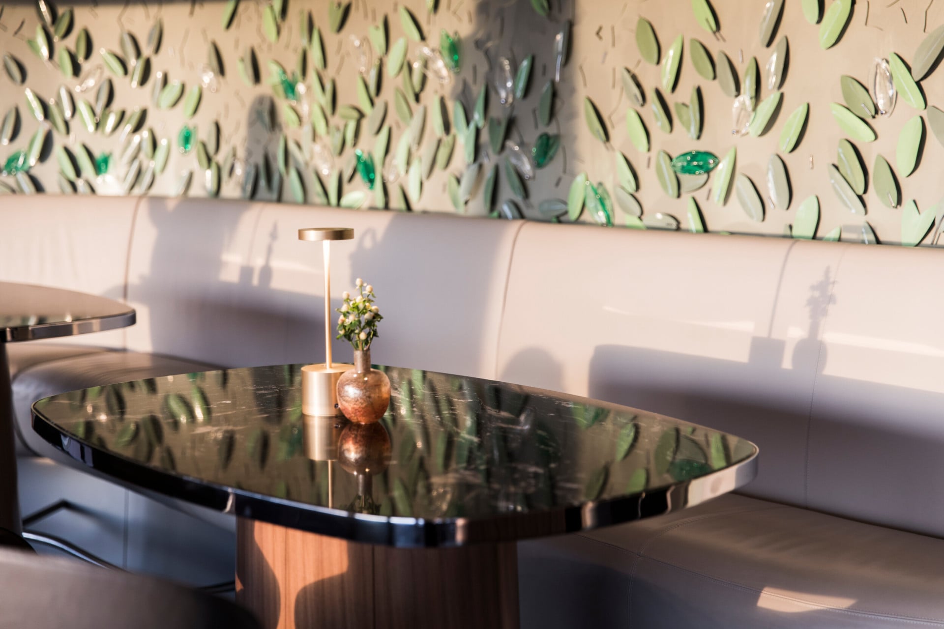 Angolo de Il Giardino bar con parete decorata con foglie di vetro e metallo e tavolo di marmo