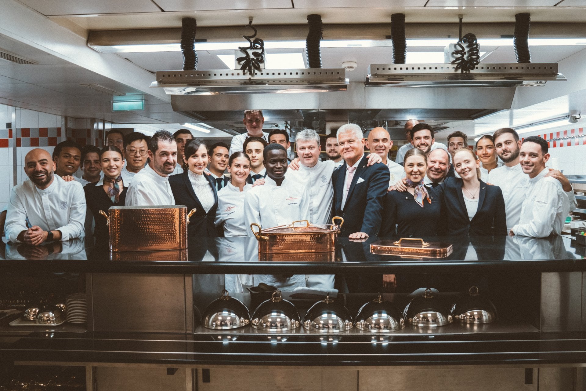 Group of people in a kitchen, posing together with chef and staff, smiling and celebrating.