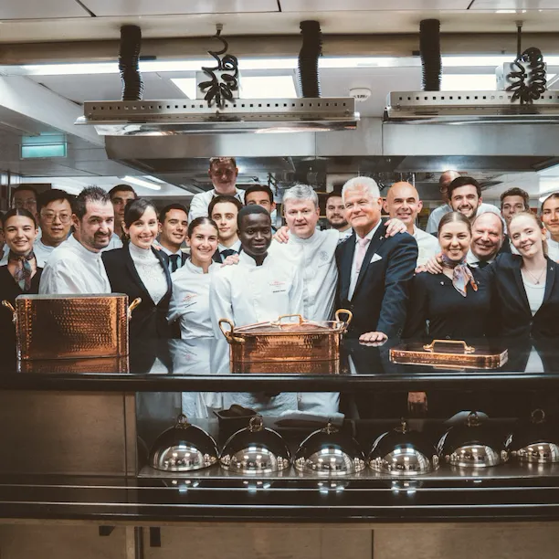 Group of people in a kitchen, posing together with chef and staff, smiling and celebrating.