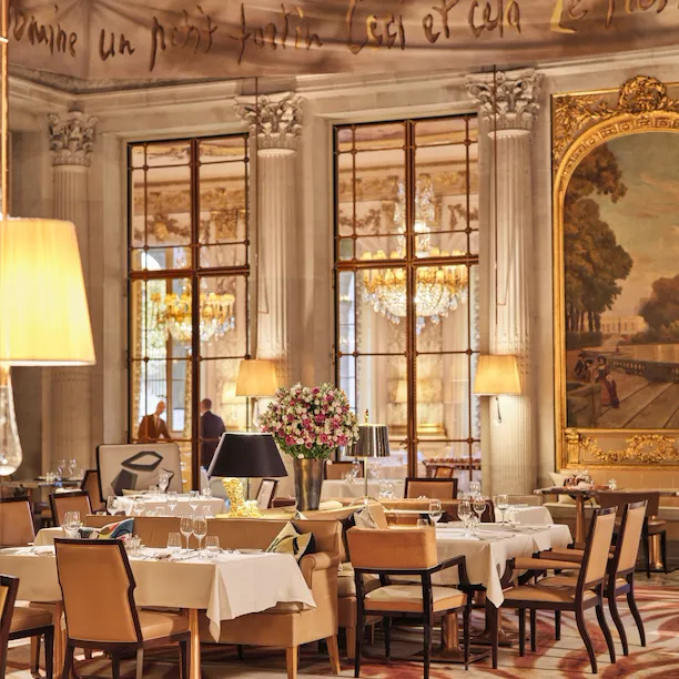 Elegant dining room with large windows, chandeliers, floral centerpiece, and polished decor.