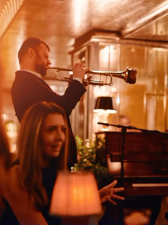 Two people playing trumpet and piano in the Vesper Bar in warm, evening light