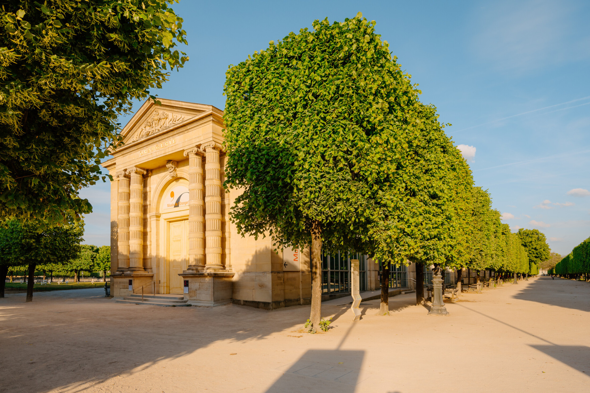 Entrance of the Musée de l'Orangerie with an alley of trees and a sunny blue sky, at Musée de l'Orangerie, Paris. 