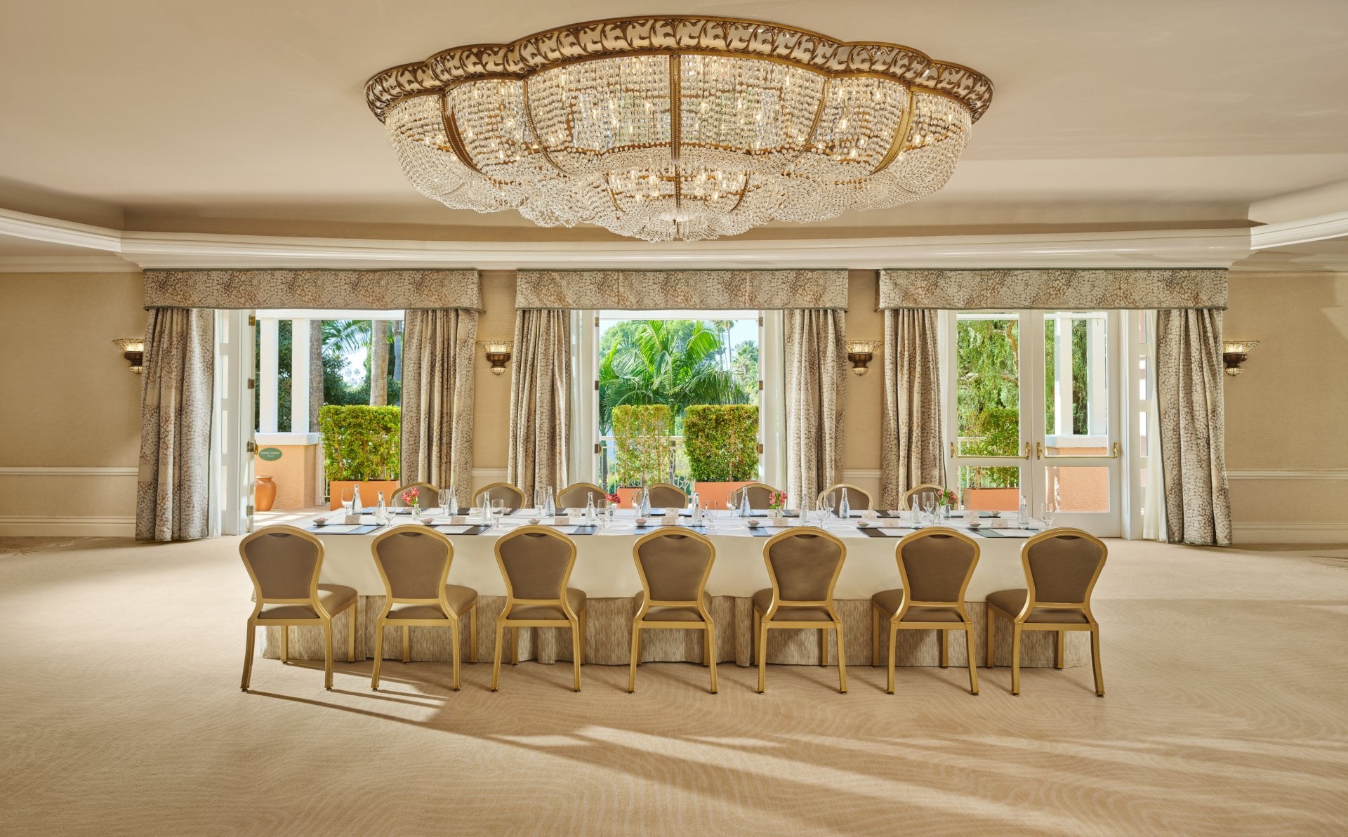 Elegant empty banquet room with large windows and a long table under a grand chandelier