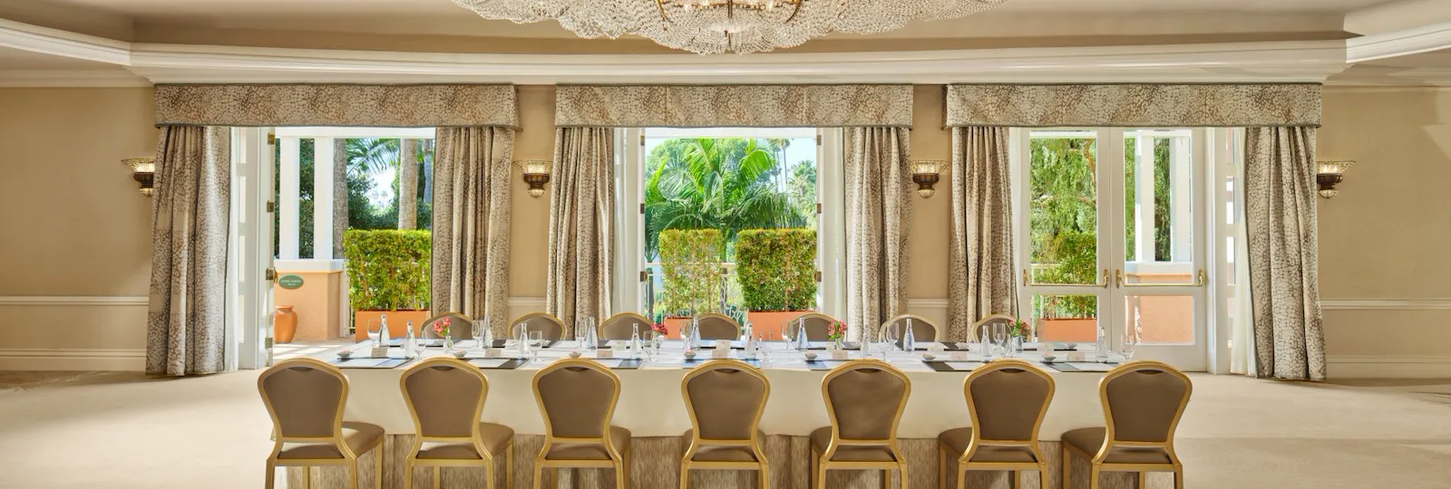 Elegant empty banquet room with large windows and a long table under a grand chandelier