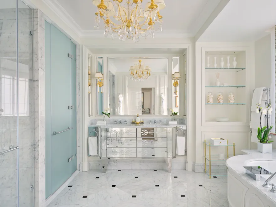 Luxurious bright bathroom with chandelier, marble surfaces, and elegant decor.